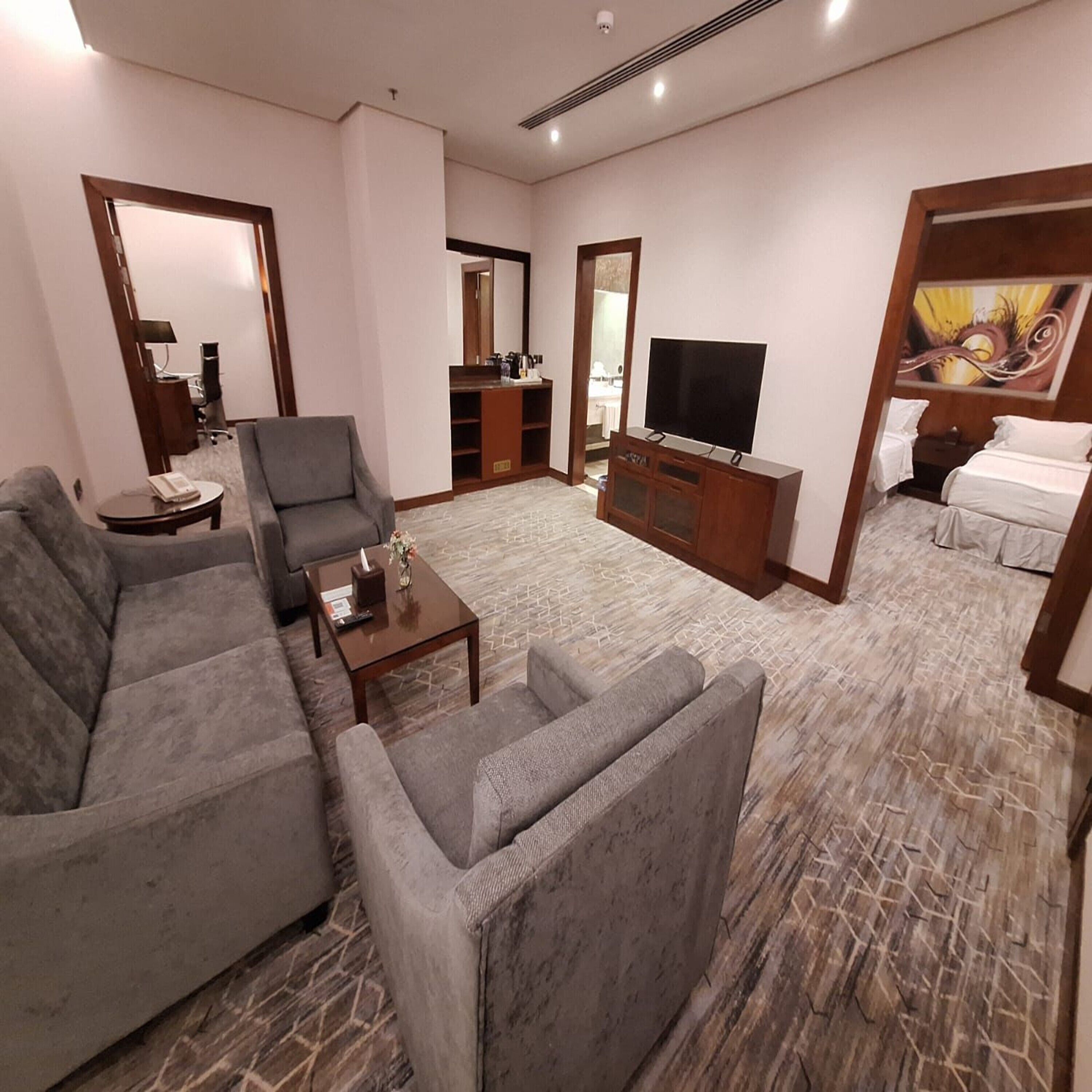 A modern living room with grey sofas, a coffee table, a TV, and a painting.