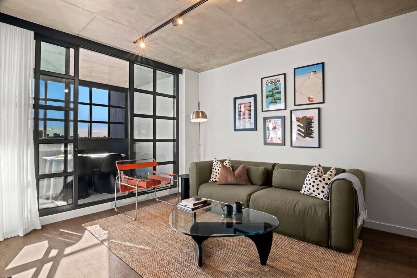 A modern living room with a large window, a sofa, a glass coffee table, and a red chair.