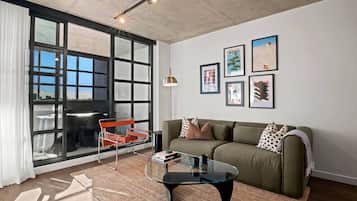 A modern living room with a large window, a sofa, a glass coffee table, and a red chair.