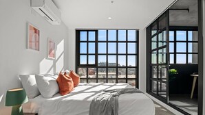 Una camera da letto moderna con una grande finestra, un letto con cuscini, una lampada da comodino e vista sulla città.