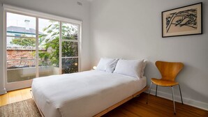 A bedroom with a bed, a chair, a window, and a framed artwork on the wall.
