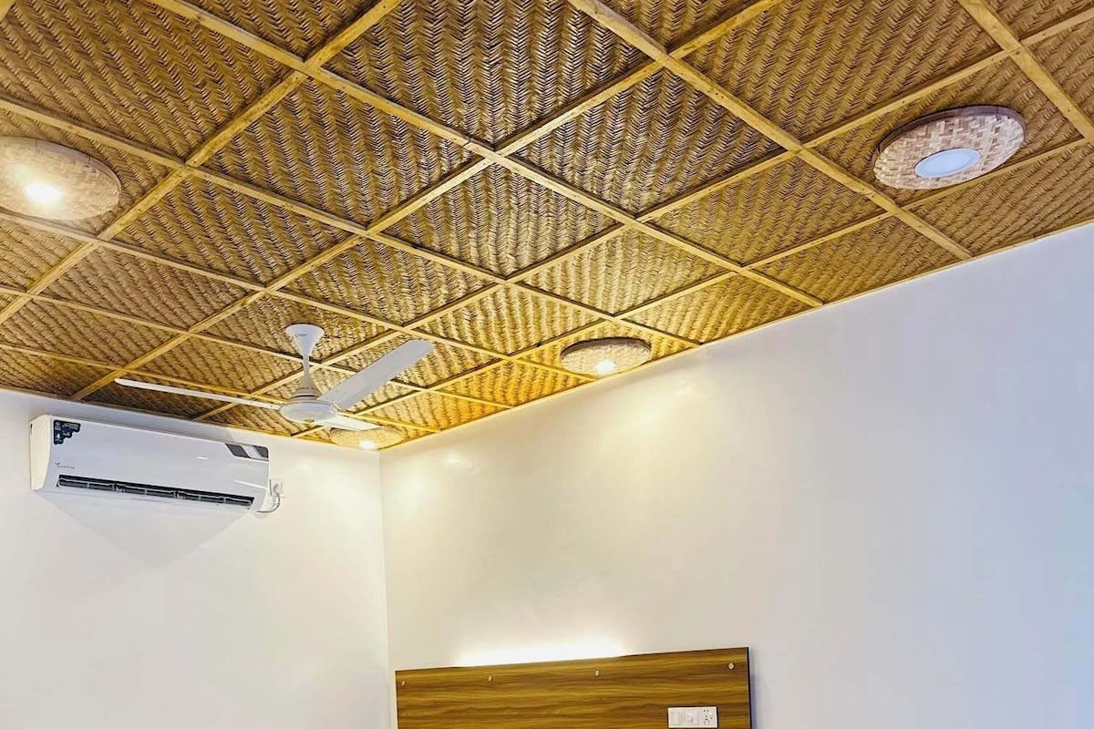 Een kamer met een bamboe plafond, een bed met een houten hoofdeinde, een nachtkastje en een airconditioning.