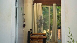 En gang der fører til en balkon med en træbænk, en ventilator og en hængende lampe.