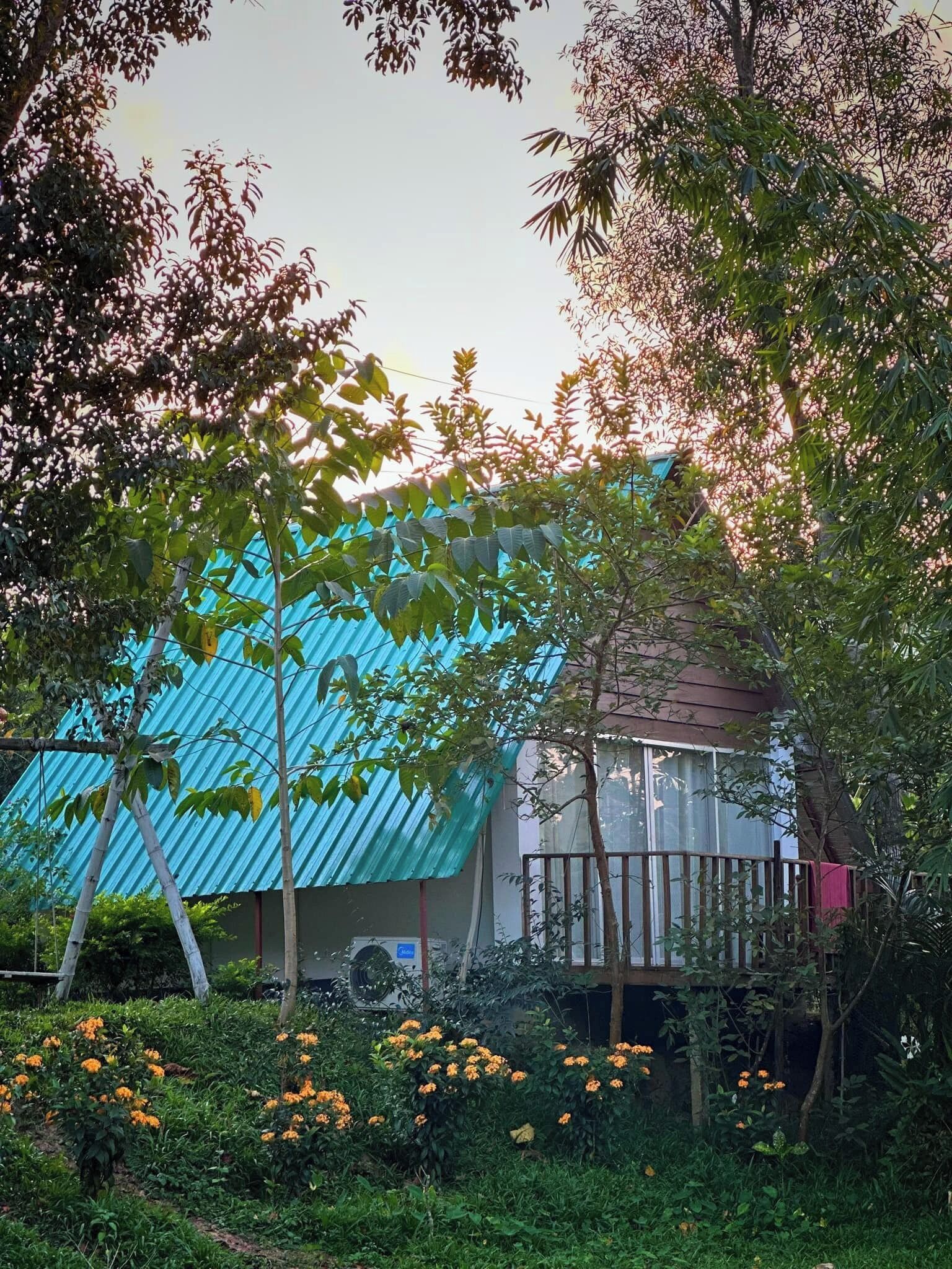Een huis met een blauw golfblikken dak, omringd door weelderig groen en bloeiende planten.