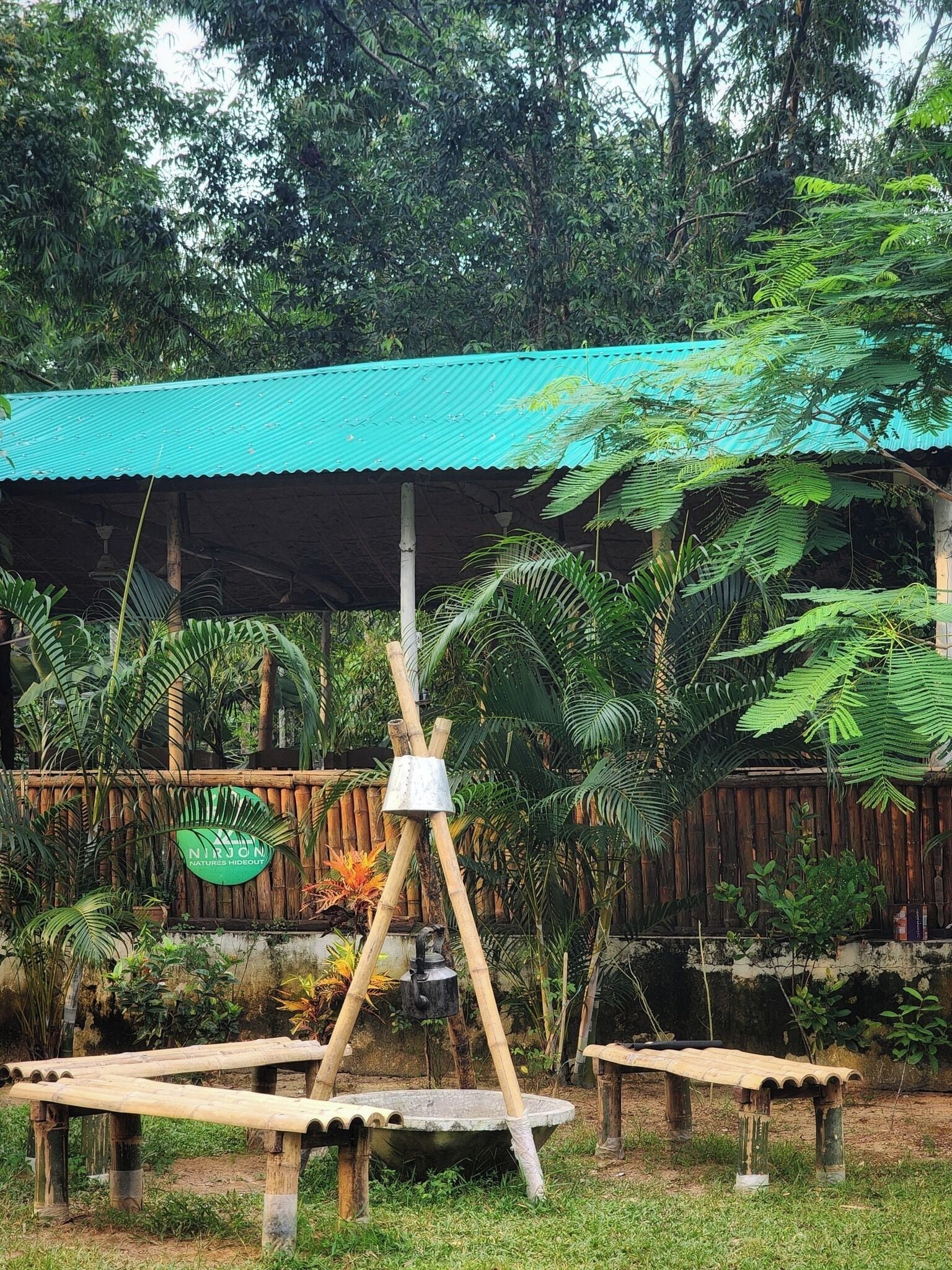 Un cadre extérieur rustique agrémenté d’une structure surmontée d’un toit végétalisé, de bancs en bois et d’une pompe à eau traditionnelle.