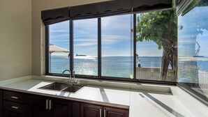 Une cuisine dotée d’une grande fenêtre donnant sur la mer, d’un évier et de meubles de rangement de couleur sombre.