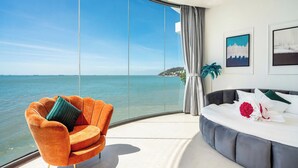 Un salon moderne doté d’une grande baie vitrée donnant sur un plan d’eau, d’un fauteuil orange moelleux, d’un canapé gris et d’un bouquet de fleurs.