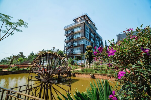 A water wheel, a modern building, and a garden with purple flowers. - Hoang Thien Homestay & Sport (Bao Loc)