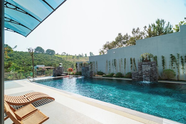 A swimming pool with a waterfall feature, surrounded by a stone wall and lush greenery.