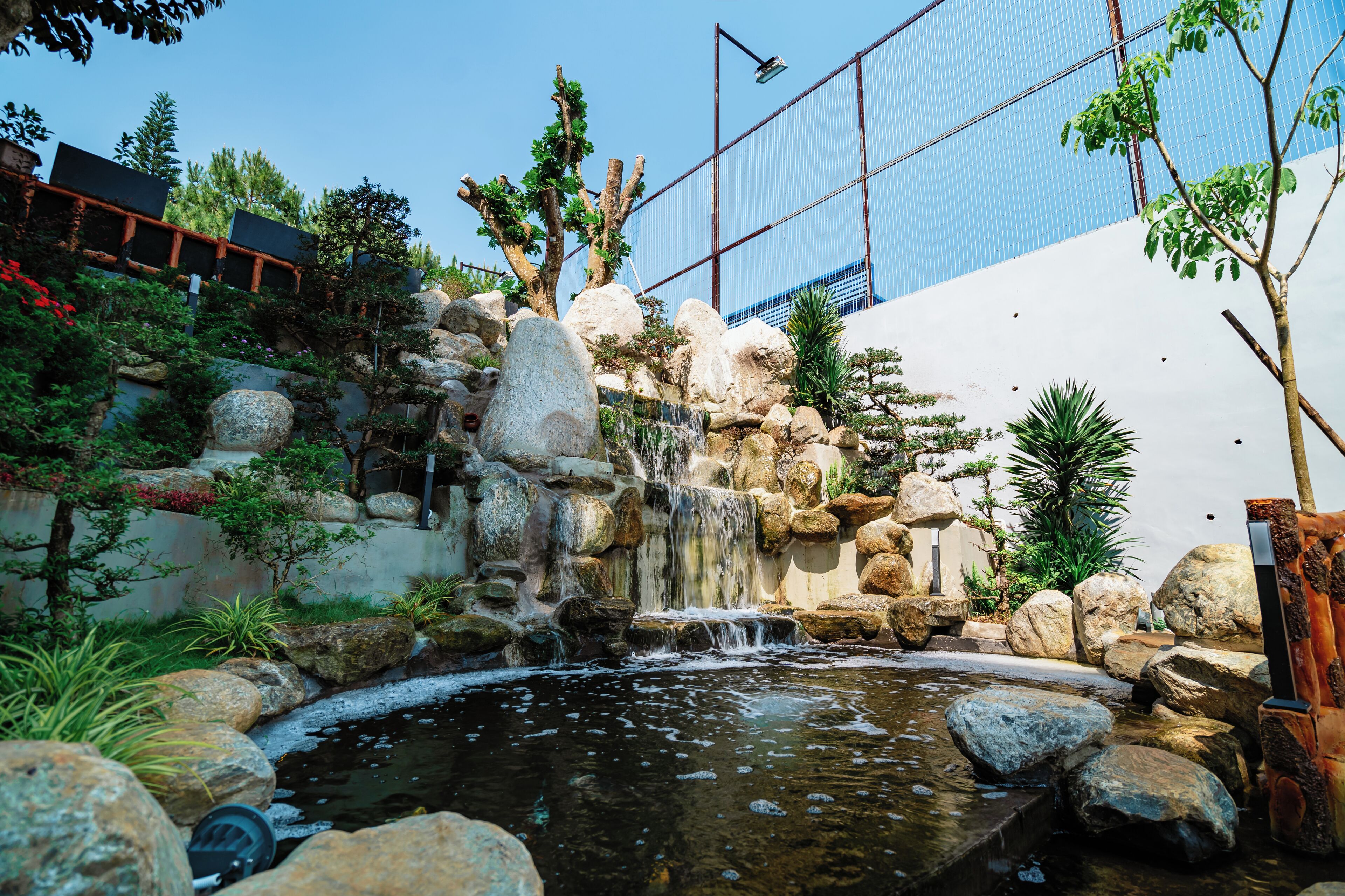 A landscaped garden with a small waterfall, rocks, and various plants.