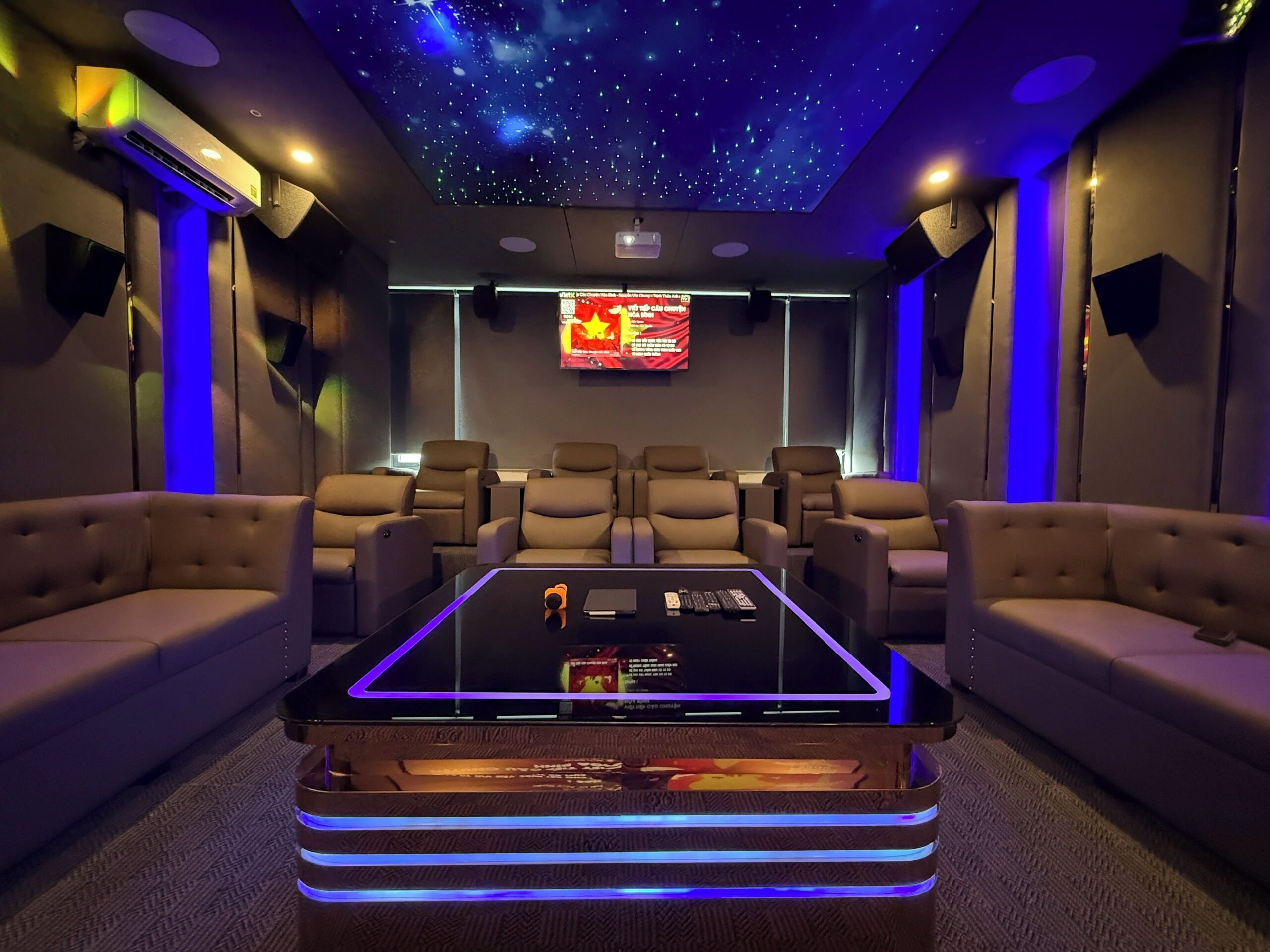 A home theater room with a starry ceiling, multiple recliner chairs, a central coffee table, and a large screen.