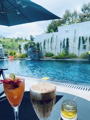 A poolside table with two drinks, a glass of iced tea with a lime slice and a straw, and a glass of iced coffee with a frothy top. - Hoang Thien Homestay & Sport (Bao Loc)