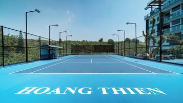Una cancha de tenis al aire libre con una red, rodeada por una cerca, y el nombre
