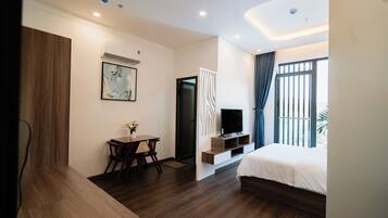 A modern hotel room with a wooden floor, a bed, a desk with a chair, a TV, and a window with curtains.