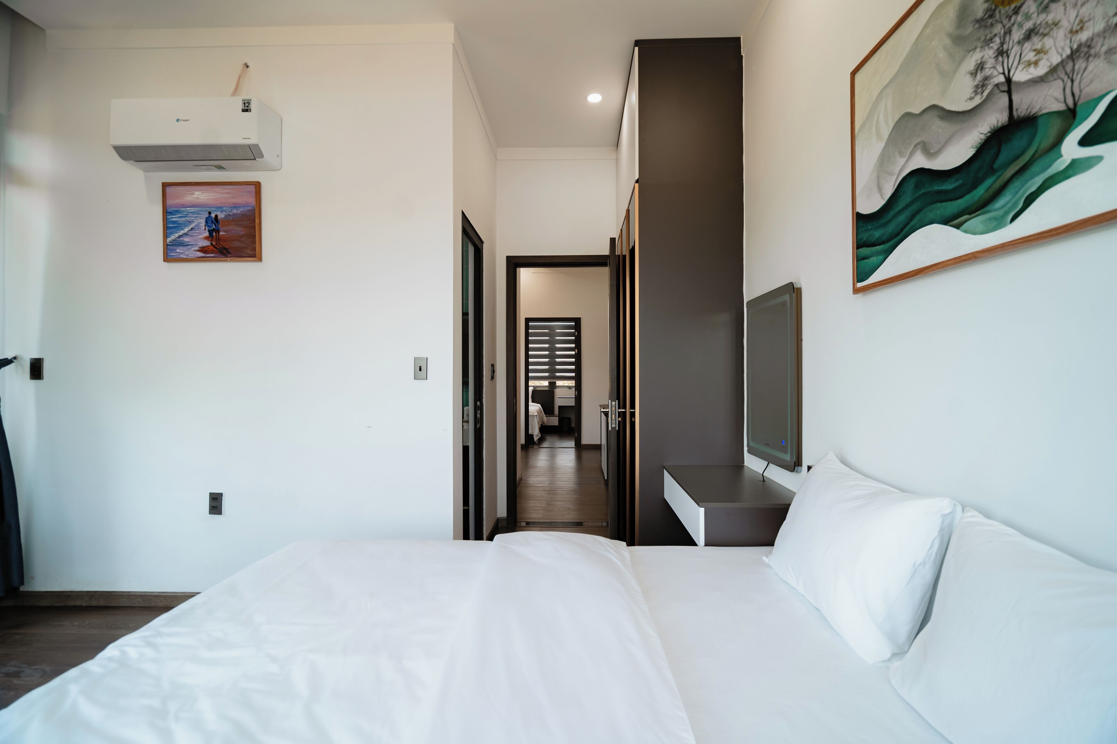 A hotel room with a bed, a TV, a painting, and an air conditioning unit.