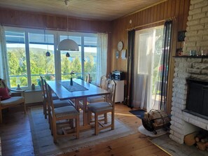 A wooden dining area with a table and chairs, a fireplace, and large windows with a view of greenery. - 7 Person Holiday Home in Kil (Kil)