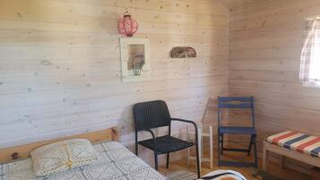 A cozy cabin room with a bed, two chairs, a small table, and a window with curtains.