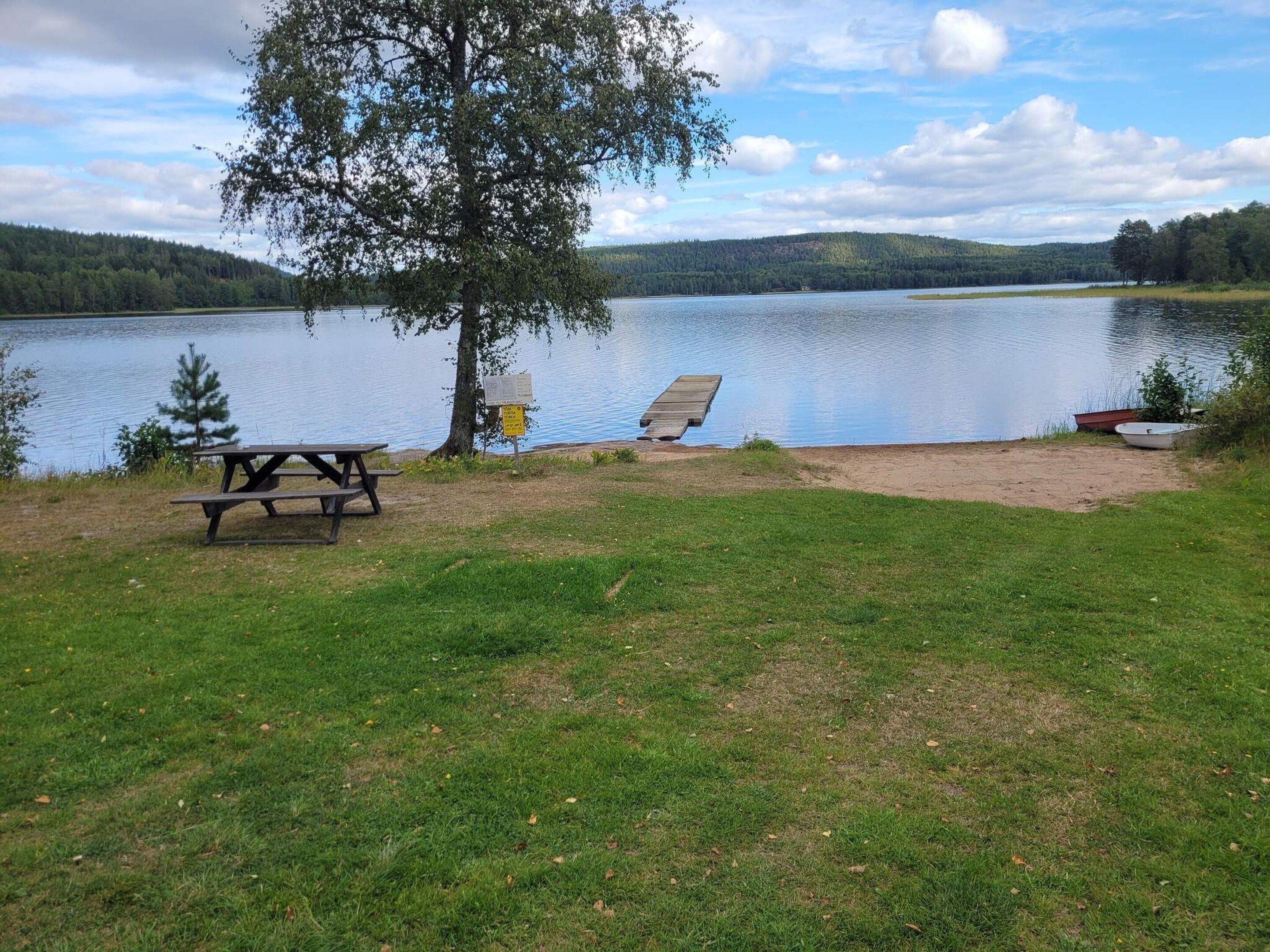 A lakeside picnic area with a bench, a picnic table, and a boat.