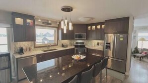 Una cocina moderna con armarios oscuros, una isla central, electrodomésticos de acero inoxidable y un amplio ventanal.