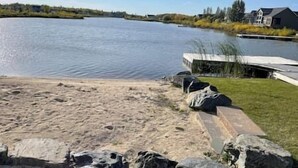 Propiedad frente al lago con playa de arena, muelle y zona verde con casas al fondo.