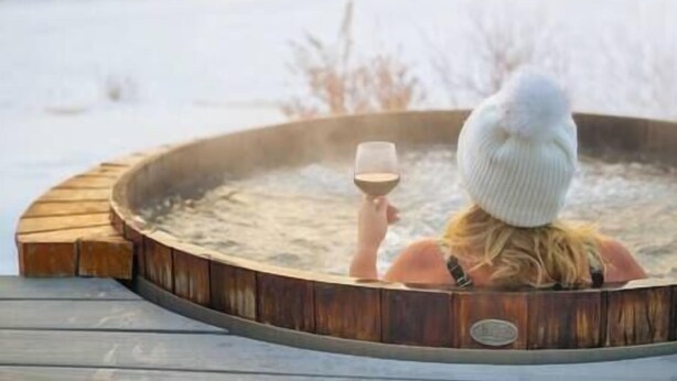 Una persona relajándose en un jacuzzi con una copa de vino, rodeada de un paisaje nevado.