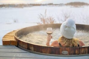 Una persona relajándose en un jacuzzi con una copa de vino, rodeada de un paisaje nevado.