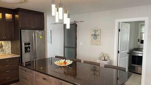 Una cocina moderna con armarios de madera oscura, un refrigerador de acero inoxidable, un horno empotrado y una isla con encimera de vidrio y fruta.