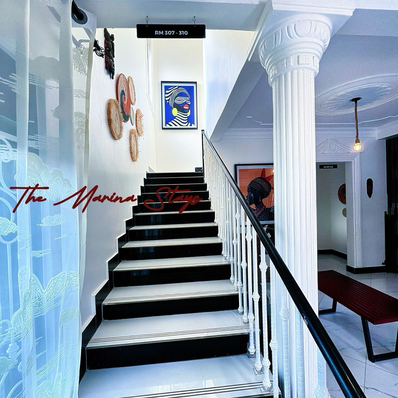 A staircase with black and white steps, white columns, and a sign above indicating room numbers RM 307 - 310.