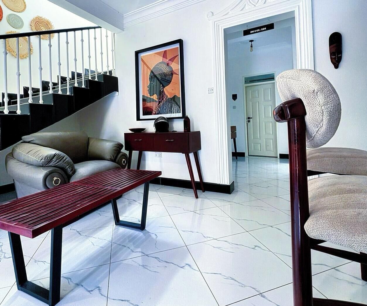 Una sala de estar moderna con sofá, una mesa de centro, una escalera y una obra de arte enmarcada en la pared.
