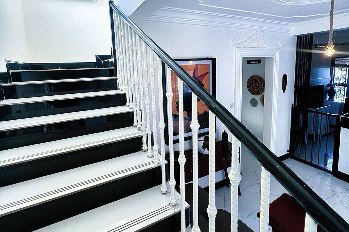 A staircase with white balusters and black steps, leading to a landing with a framed artwork and a door labeled "The Marina Stays".
