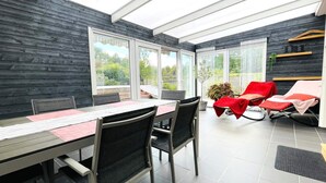 Un espace repas moderne avec une paroi en verre, une table avec des chaises et un coin salon avec des chaises rouges.