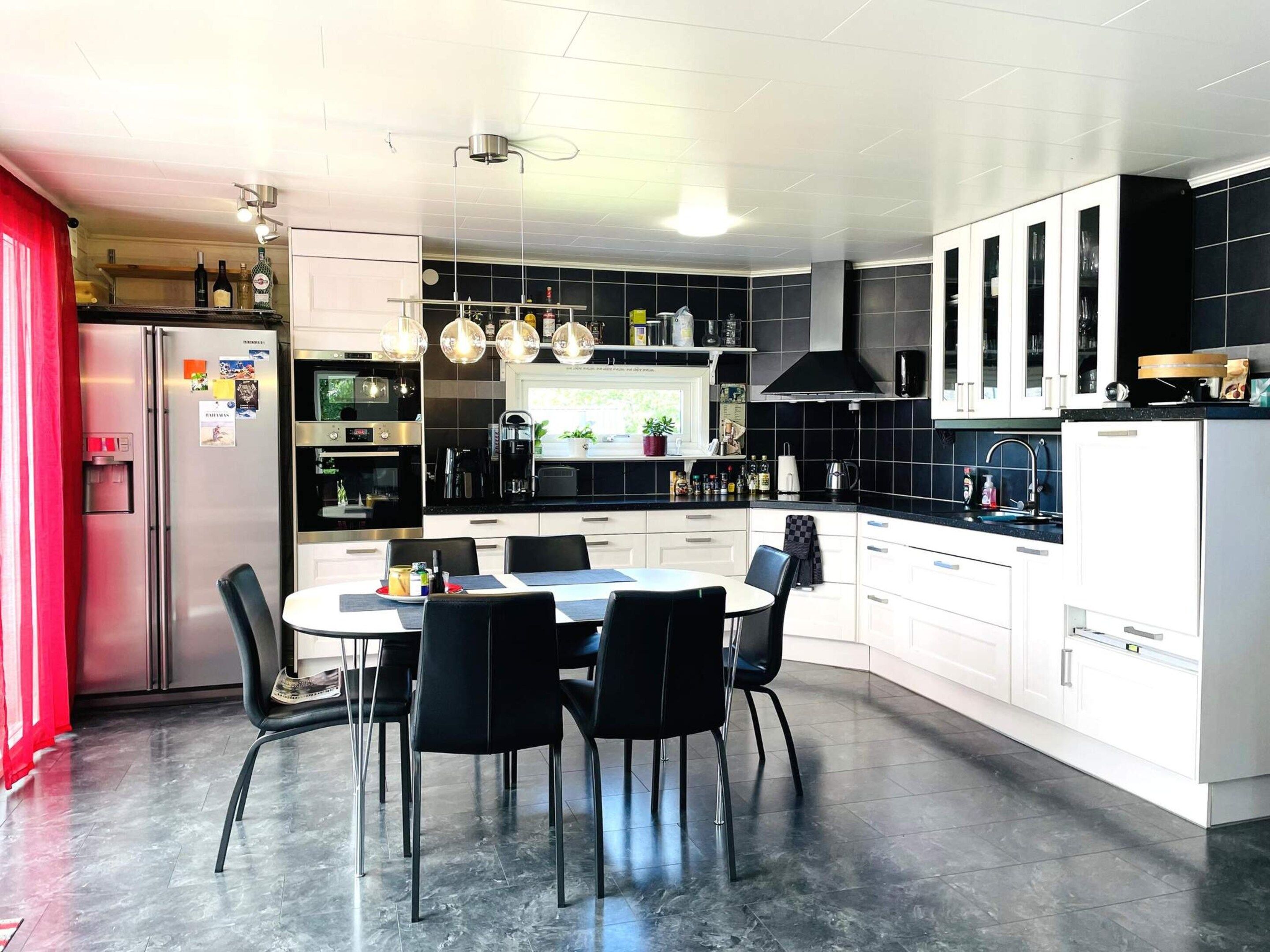 Una cocina moderna con comedor, que incluye refrigerador, horno y salpicadero de azulejos negros.