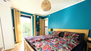 Une chambre avec un grand lit, une tête de lit en bois, une fenêtre avec des rideaux et un luminaire au plafond.