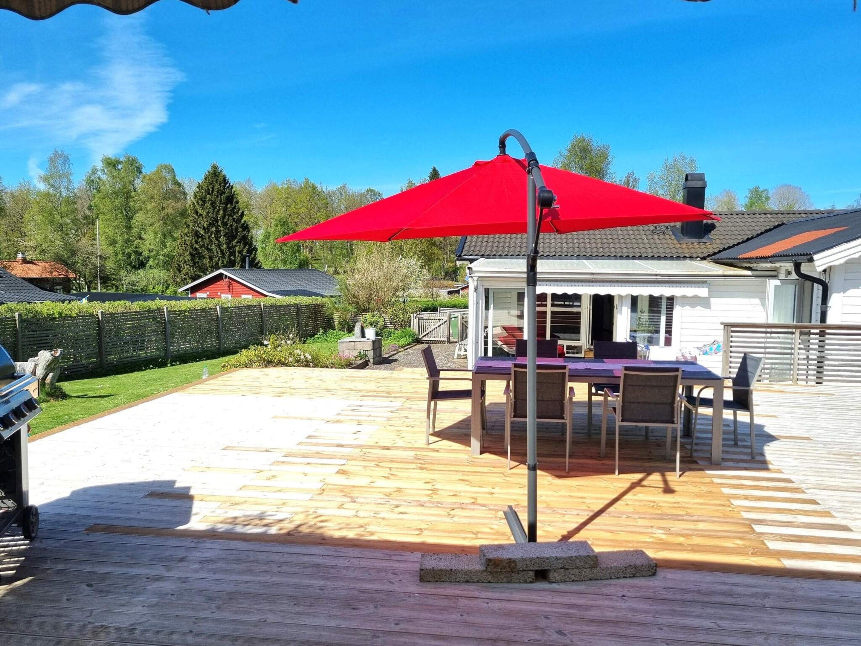 A wooden deck with a red umbrella, outdoor furniture, and a view of a house in the background.