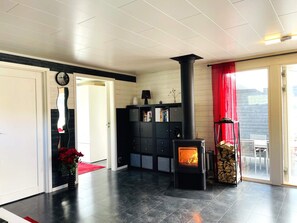 Ett modernt vardagsrum med en öppen spis, ett svart skåp med lådor, en röd gardin och en klocka på väggen.