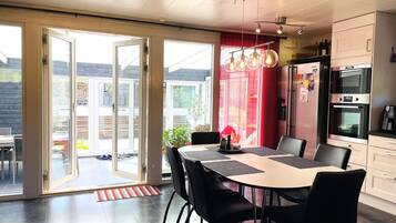 A modern kitchen with a dining area, featuring a large table with chairs, a refrigerator, and an oven.