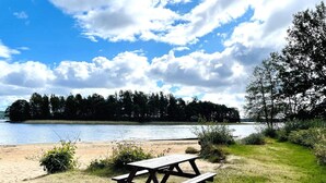 Une table de pique-nique au bord d’un lac, avec une zone herbeuse et des arbres en arrière-plan.