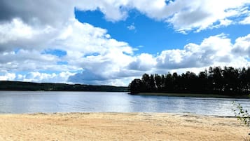 A beach with a sandy shore and a calm lake under a partly cloudy sky.