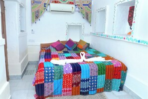 Un dormitorio pequeño y acogedor con una colcha de patchwork colorida, una toalla blanca y una disposición de toallas en forma de corazón.