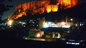 A historic fort with illuminated walls at night, surrounded by a town with visible buildings and streetlights. - Jodhpur Heritage Haveli (Jodhpur)