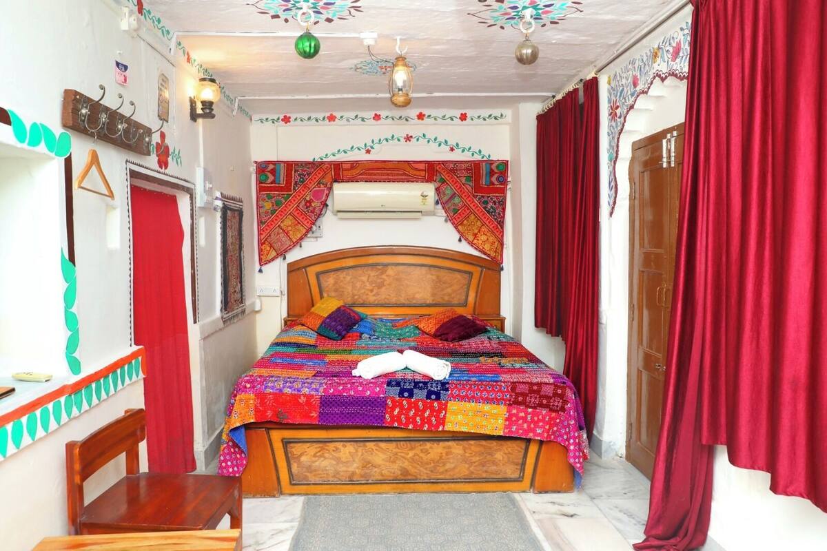 A room with a wooden bed, colorful quilts, and red curtains.