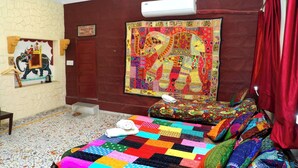 A room with a colorful quilted bedspread, a large embroidered tapestry on the wall, and a small rug on the floor. - Jodhpur Heritage Haveli (Jodhpur)