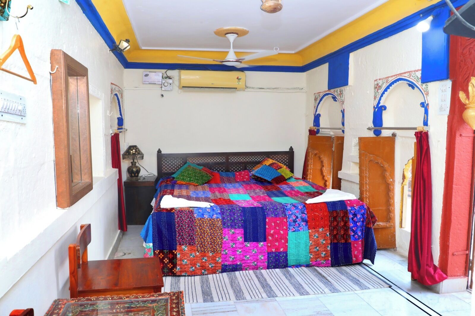 A bedroom with a colorful quilt, a wooden bed frame, a small table, and a ceiling fan.