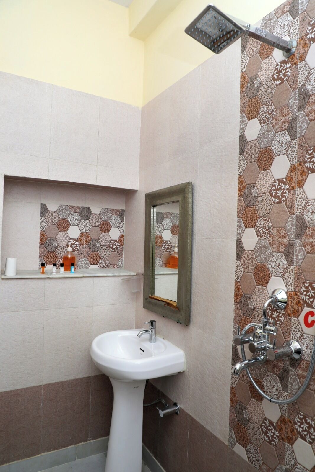 Une salle de bain avec un lavabo blanc, un miroir et une douche dont le mur est recouvert de carreaux à motifs.