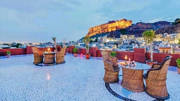 An outdoor seating area with wicker furniture and a view of a historic fort. - Jodhpur Heritage Haveli (Jodhpur)
