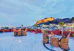 An outdoor seating area with wicker furniture and a view of a historic fort. - Jodhpur Heritage Haveli (Jodhpur)