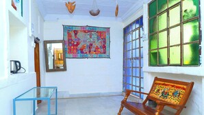 A room with a glass table, a wooden chair with a colorful seat, a tapestry with an elephant design, and a window with green-tinted glass. - Jodhpur Heritage Haveli (Jodhpur)