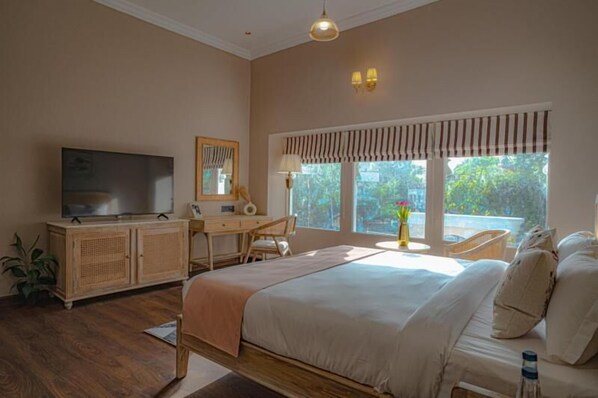 Un dormitorio con cama, escritorio, televisor y ventana con cortinas.