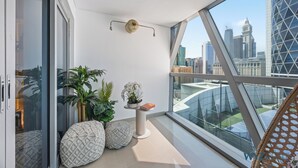 Un balcon moderne offrant une vue sur la ville, agrémenté d’une plante en pot, d’une petite table avec un livre et d’un coussin aux motifs géométriques.