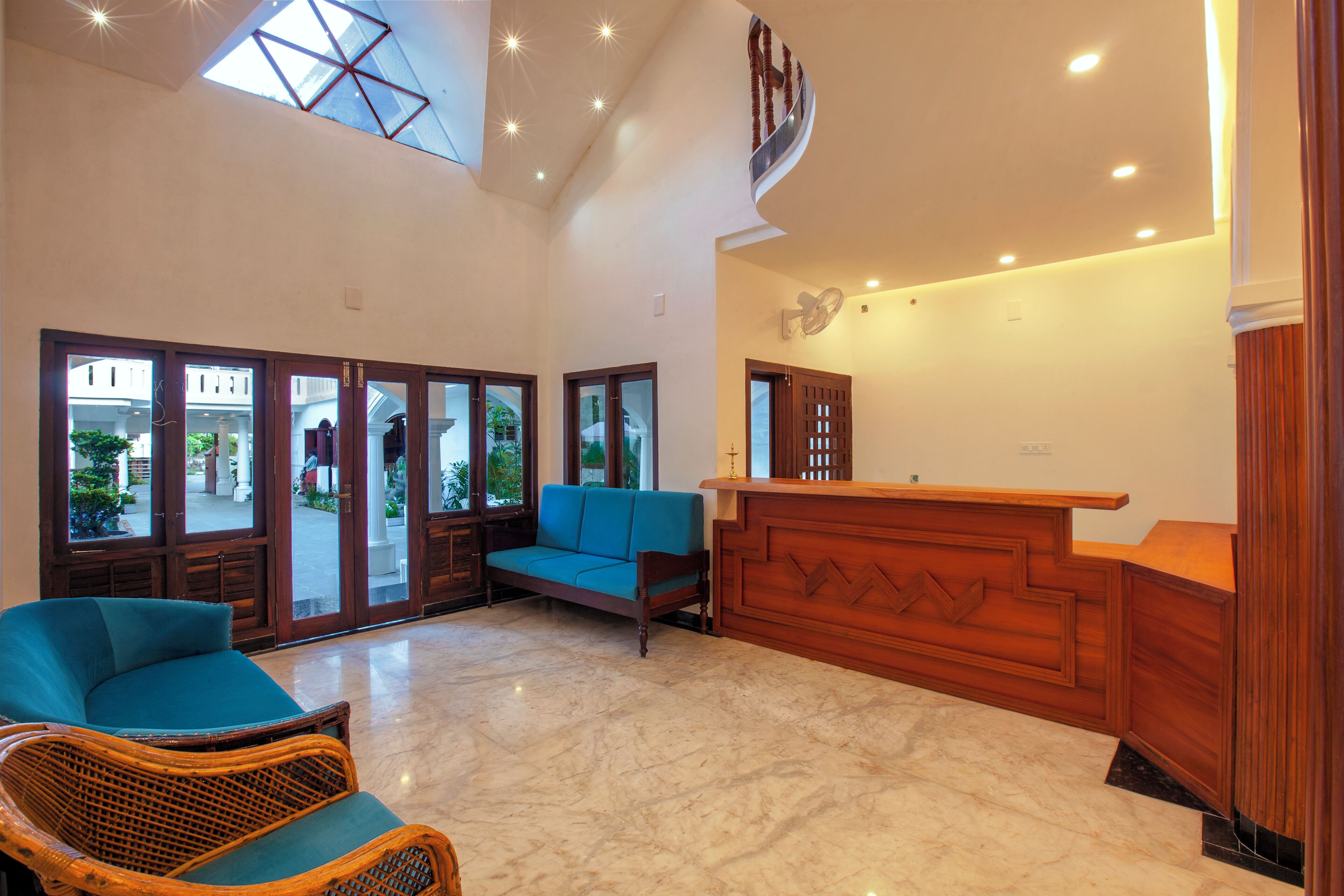 A spacious lobby with a high ceiling, a reception desk, a blue sofa, and a wicker chair.